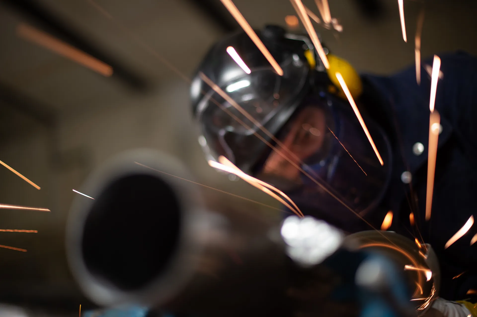 Soudeur derrière sa visière projetant des étincelles sur une tuyauterie industrielle, gros plan