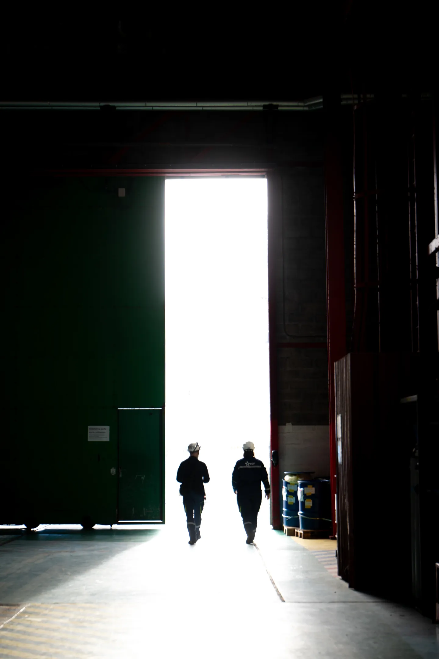 Silhouettes de deux techniciens casqués marchant vers la lumière dans le portail d'une salle des machines