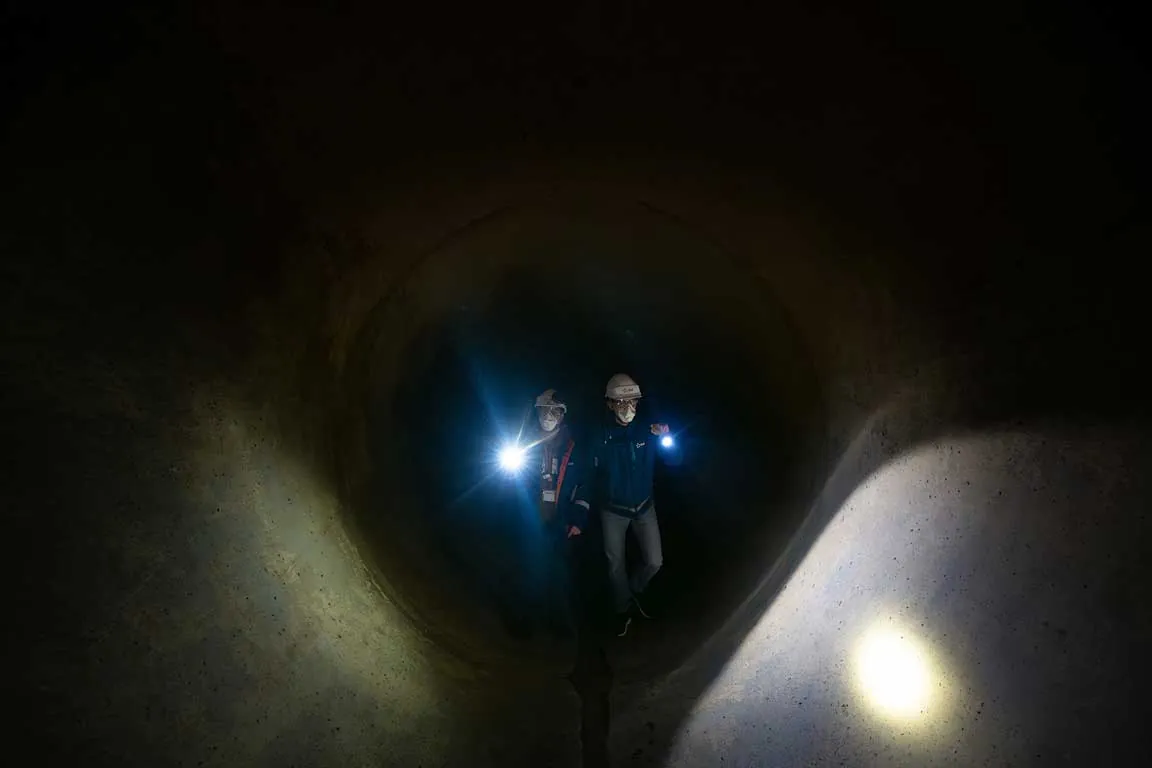 Deux techniciens équipés de lampes frontales progressant dans une conduite souterraine de centrale nucléaire