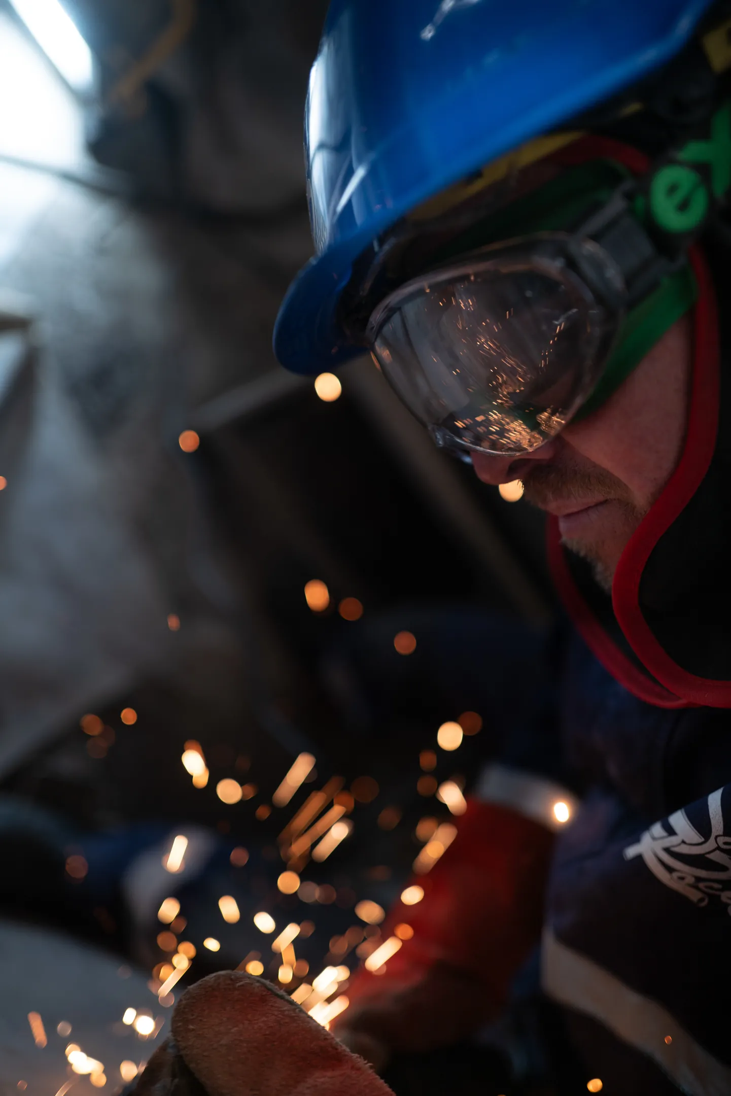 Gros plan d'un soudeur en casque bleu et lunettes de protection, bokeh d'étincelles dorées