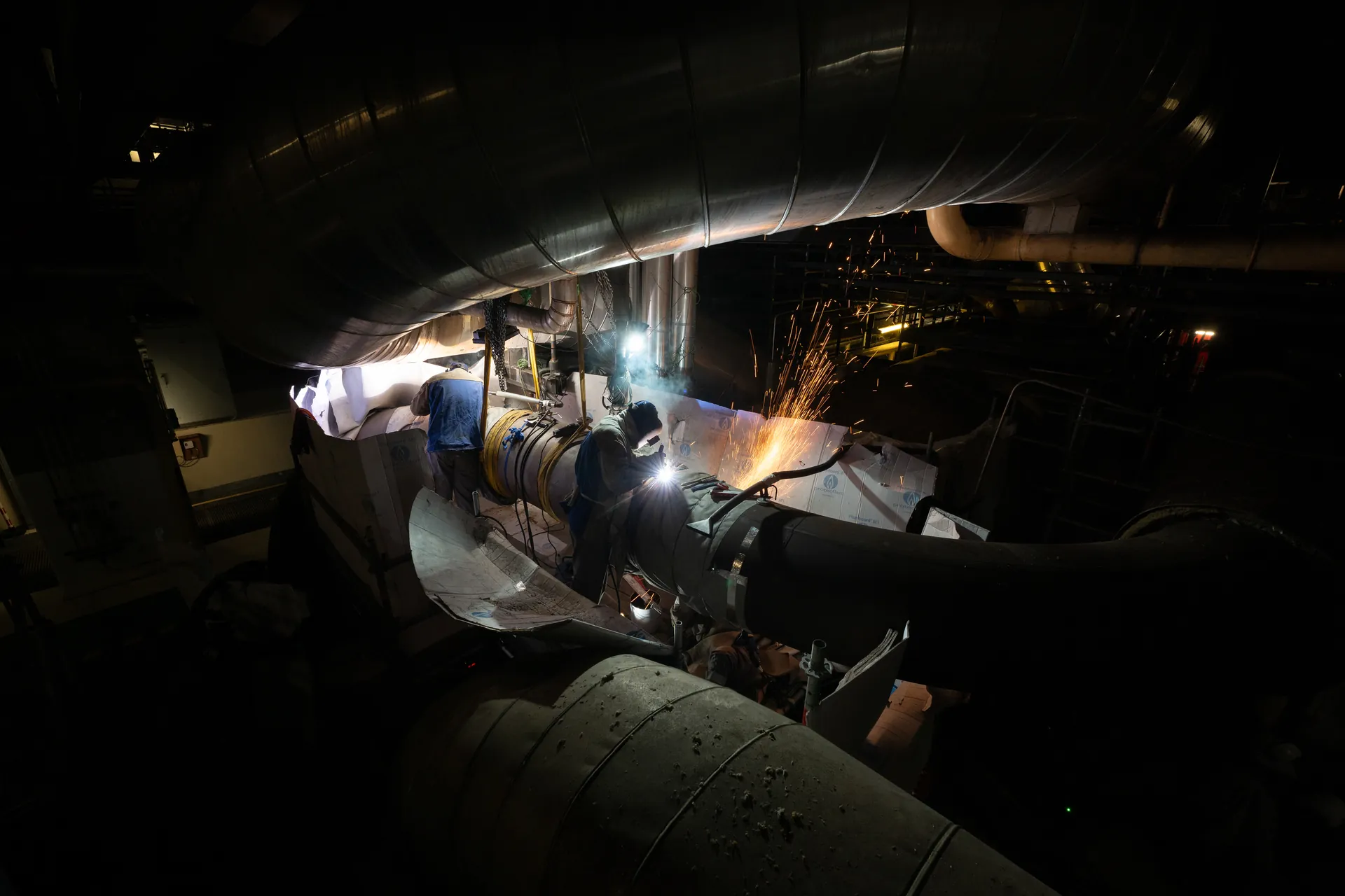 Soudeurs travaillant de nuit sur une tuyauterie dans le bâtiment réacteur, arc de soudure et étincelles
