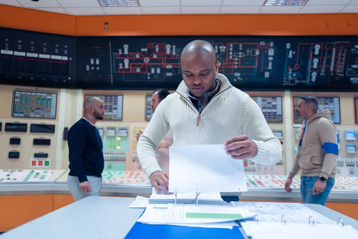 Opérateur consultant des documents en salle de commande nucléaire, collègues en arrière-plan