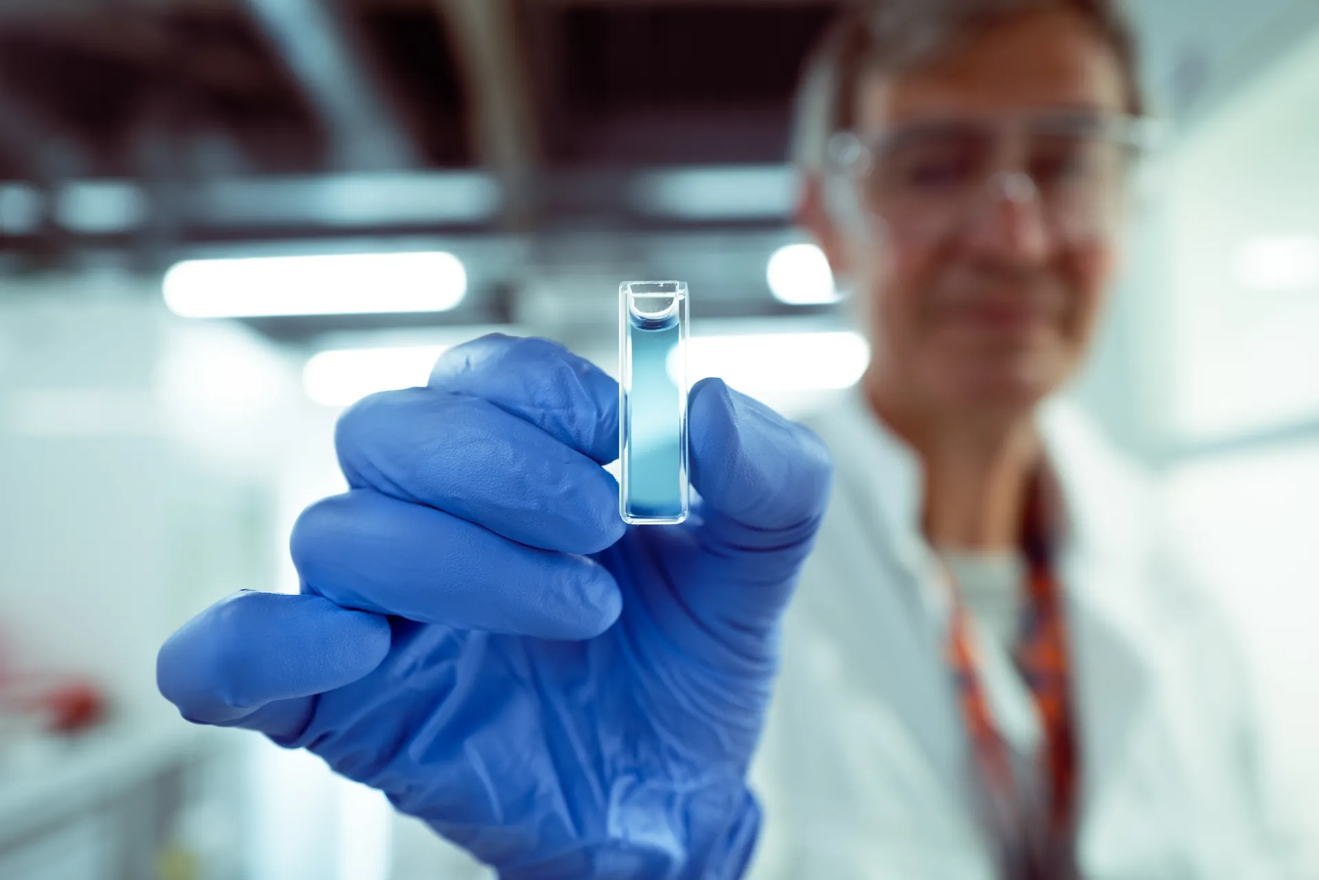 Technicienne en gants bleus présentant une cuvette d'analyse dans un laboratoire industriel