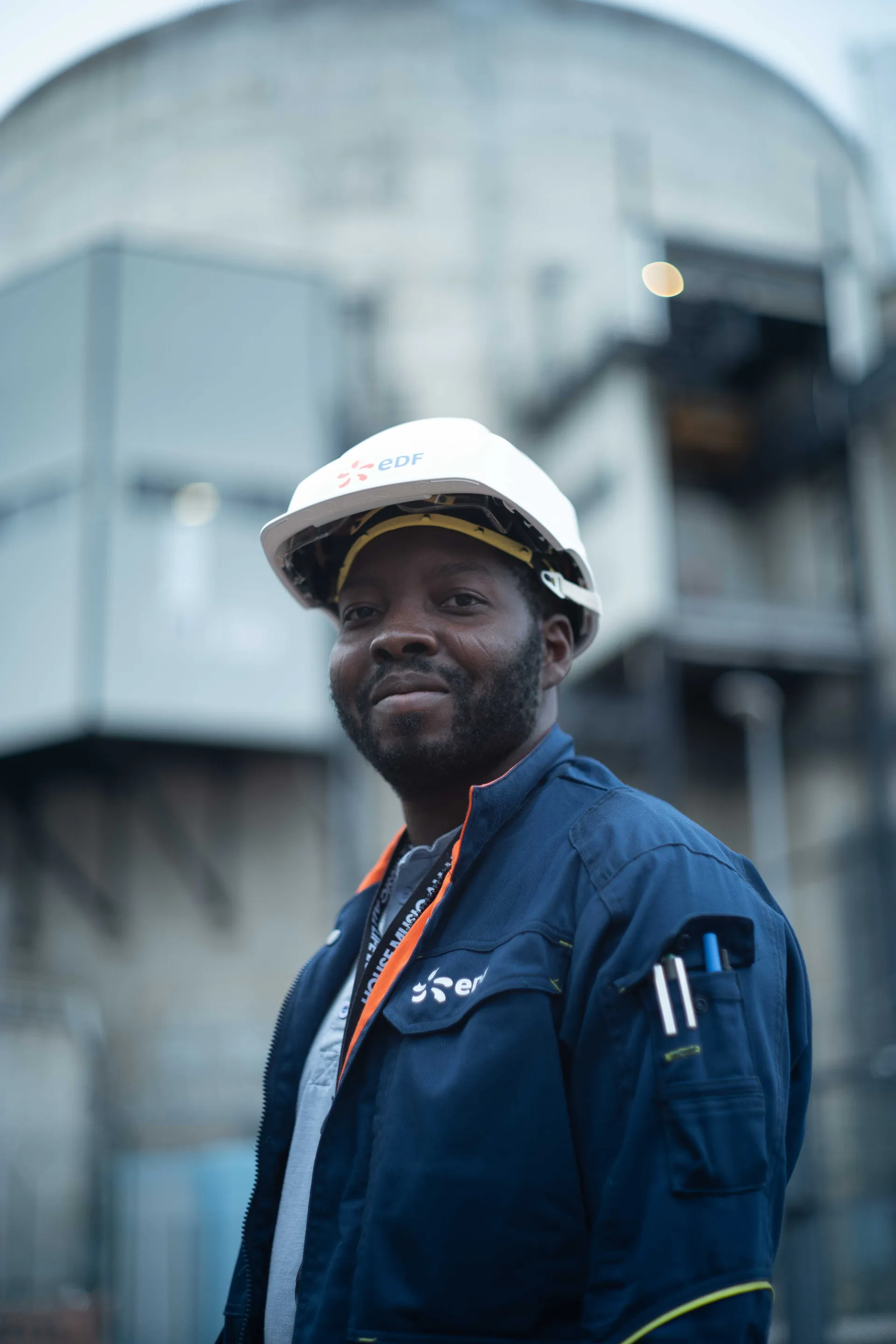 Technicien EDF en casque blanc et combinaison bleue devant le bâtiment réacteur d'une centrale nucléaire