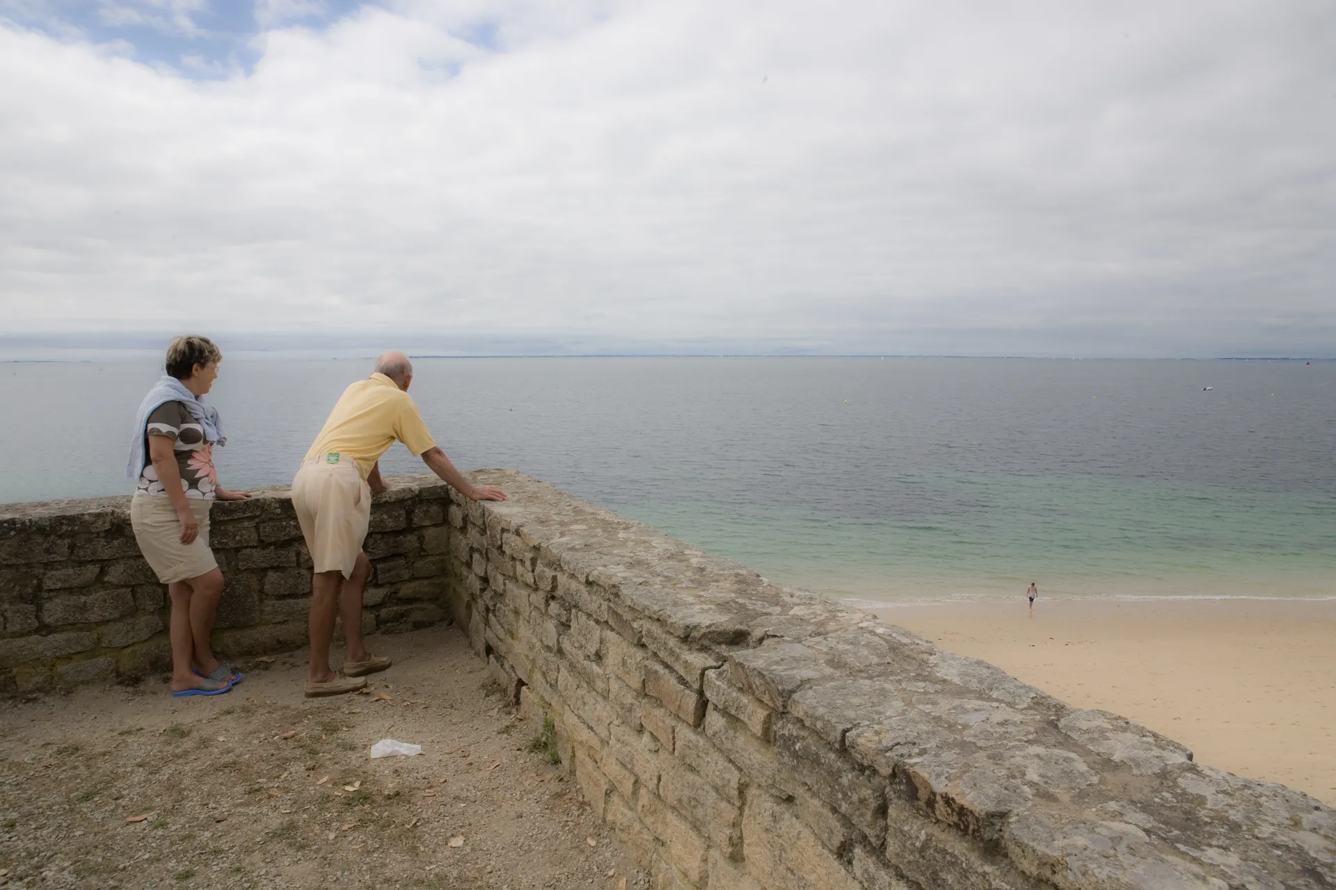 Femme en robe de chambre rayée marchant de dos dans un chemin creux entre deux dunes vers la mer