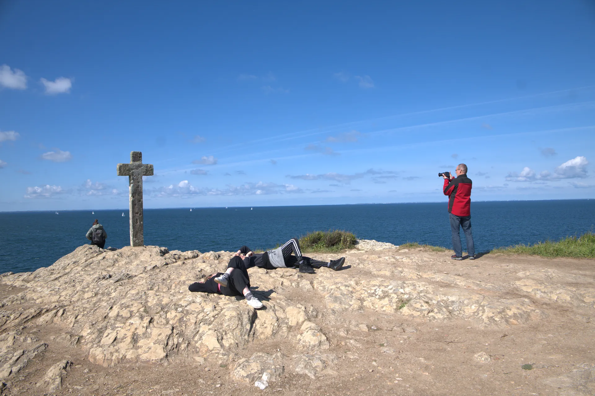 Famille assise sur un muret de pierre consultant une carte, voiliers en arrière-plan