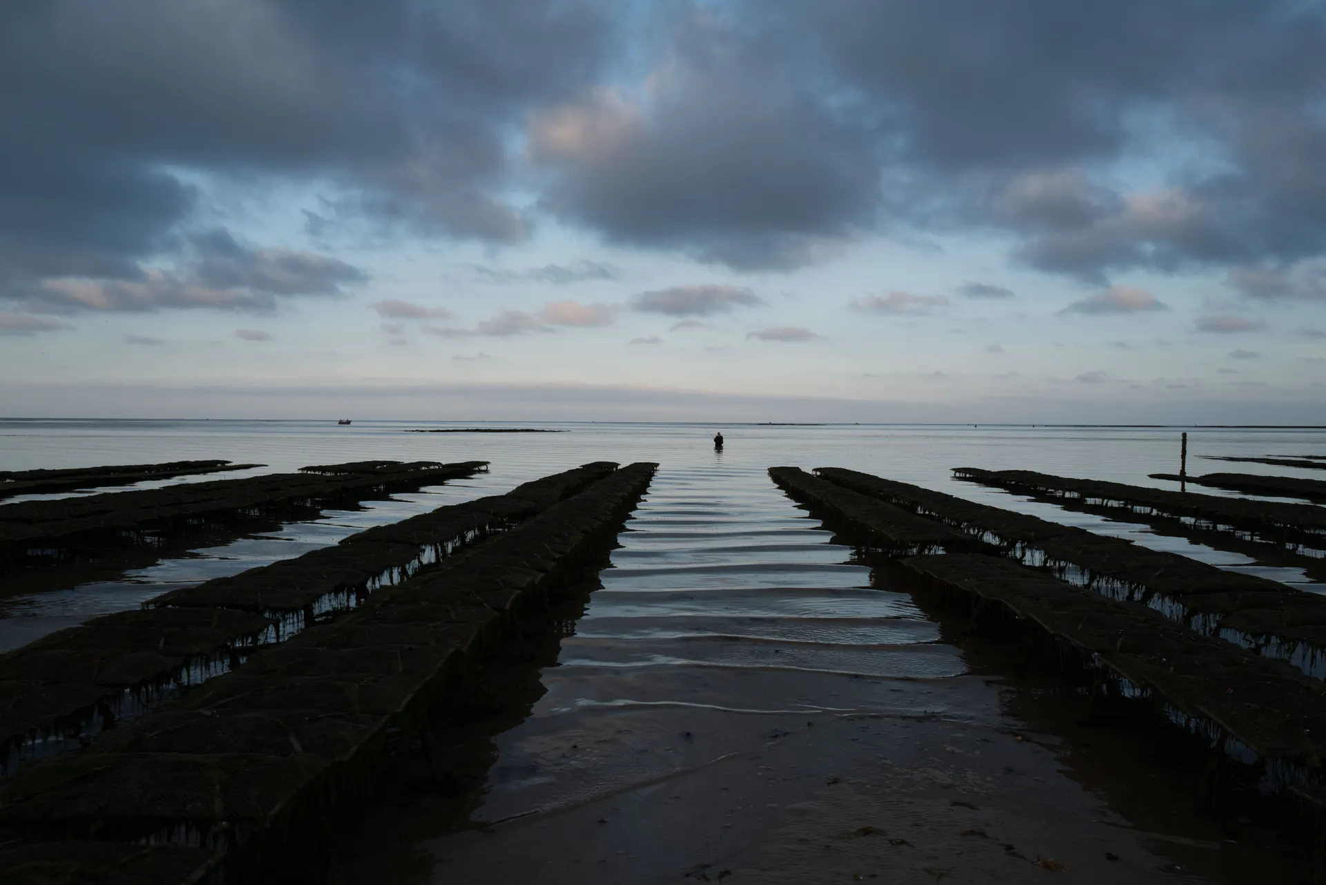 Femme en noir pieds nus au bord de l'eau, main dans les cheveux, face à la mer turquoise