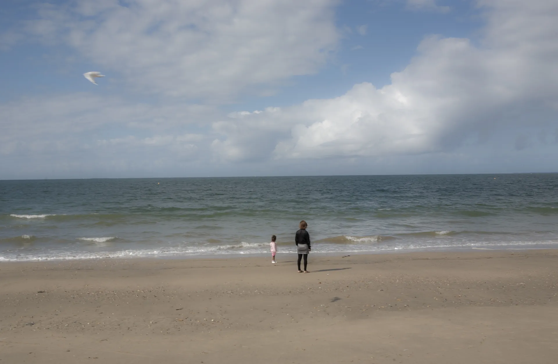 Silhouette entrant dans les vagues en contre-jour argenté, bateaux et fort en arrière-plan